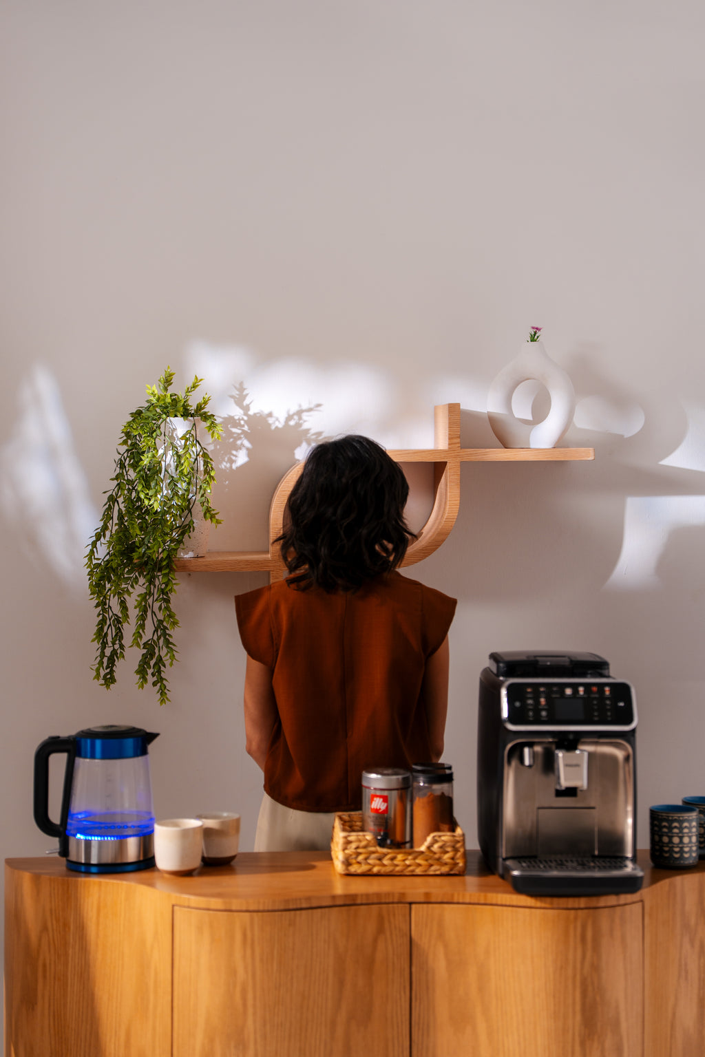 Person standing in a kitchen with a coffee machine and shelves. showing coffee corner made from natural wood 