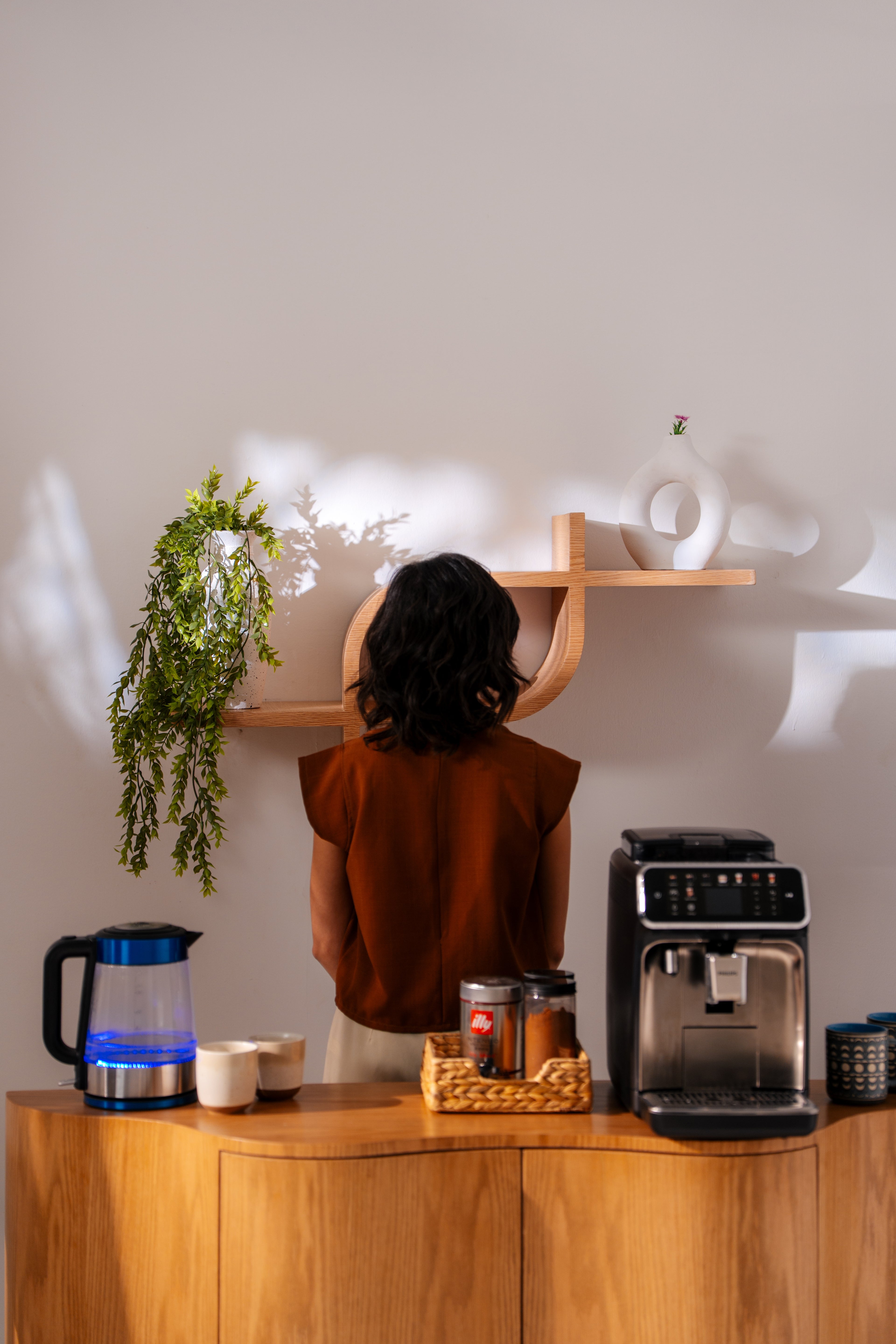 Person standing in a kitchen with a coffee machine and shelves. showing coffee corner made from natural wood 